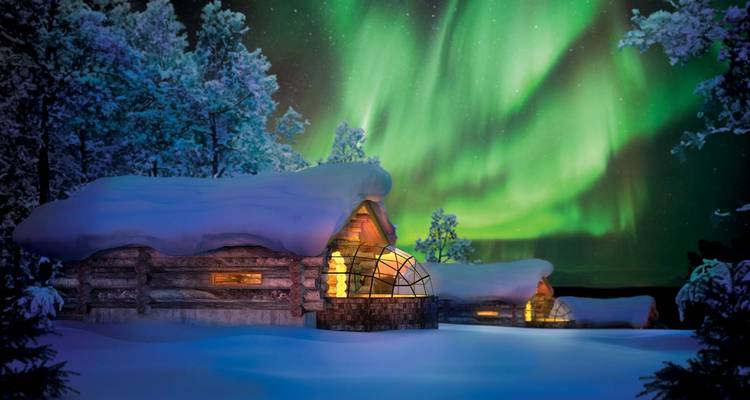 Noorderlicht boven besneeuwde hutten in een bos.