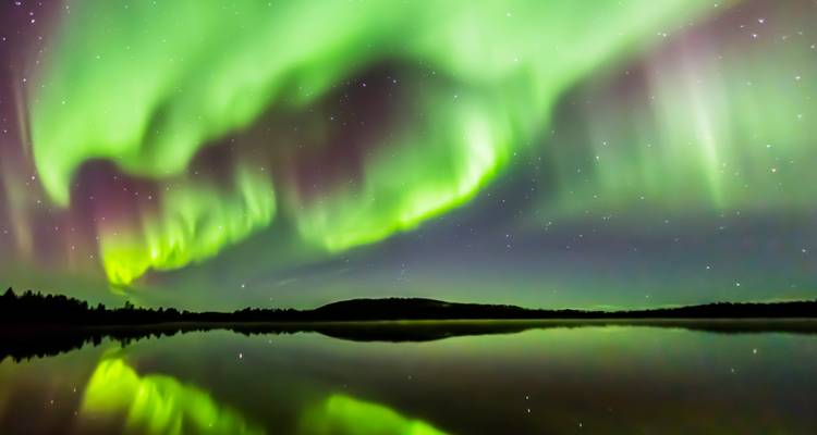 Noorderlicht weerkaatsend over een kalm meer 's nachts.