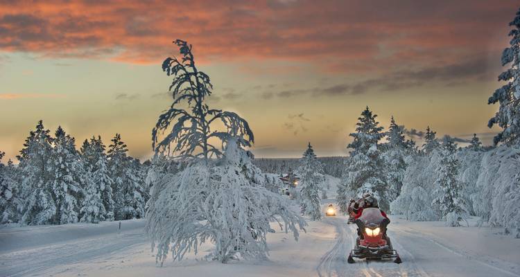 Sneeuwscootertocht door een besneeuwde bos bij zonsondergang.