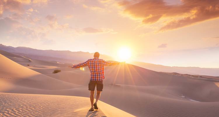Mann, der den Sonnenaufgang über Sanddünen umarmt.