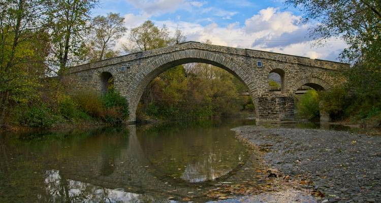 Een stenen brug over een kalme rivier omgeven door herfstgebladerte.