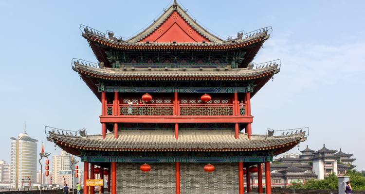 Traditioneller Trommelturm auf den Stadtmauern von Xi'an mit roten Laternen und moderner Skyline im Hintergrund.