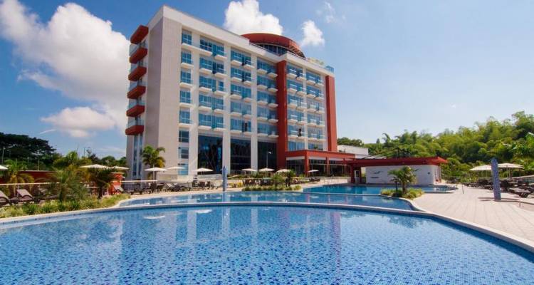 Ein modernes Hotelgebäude mit einem Schwimmbad davor, umgeben von Grünflächen.