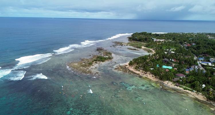 Vue aérienne d'une île avec des vagues qui se brisent sur le rivage et une structure semblable à un pont s'étendant dans l'océan.