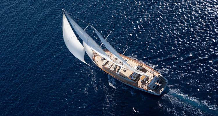 Vue aérienne d'un yacht à voile fendant les eaux d'un bleu profond.