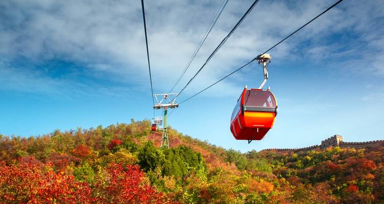 Téléphériques se déplaçant au-dessus d'une forêt d'automne colorée avec une section de la Grande Muraille de Chine.
