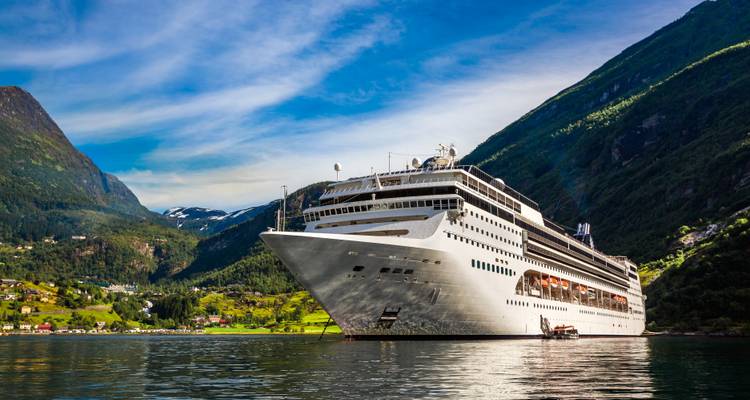 Großes weißes Kreuzfahrtschiff vor Anker in einem ruhigen Fjord, umgeben von hohen grünen Bergen unter klarem Himmel.