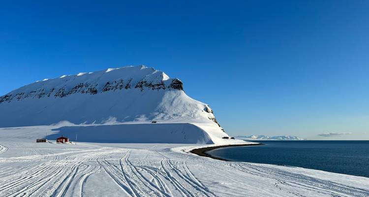 Isolierte schneebedeckte Landzunge, die auf das dunkelblaue Nordpolarmeer unter wolkenlosem Himmel trifft.