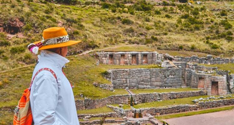 Touriste observant des ruines de pierre sur un paysage herbeux.