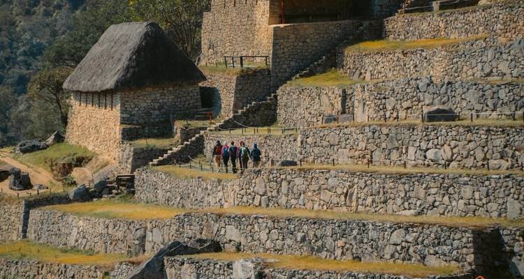 Groupe de randonneurs marchant le long de terrasses en pierre et d'une structure au toit de chaume.