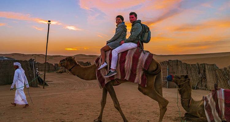 Twee mensen die op kamelen rijden bij zonsondergang in een woestijn.