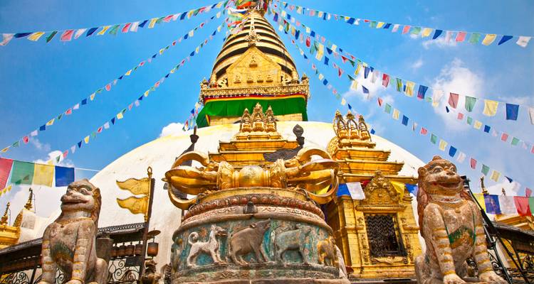 Swayambhunath Stupa mit Gebetsfahnen und Wächterstatuen vor einem klaren blauen Himmel.