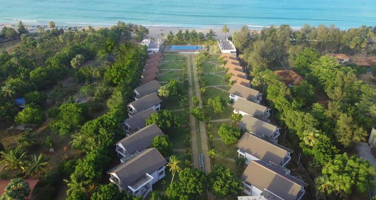 Luftaufnahme eines Resorts mit einem Pool direkt am Strand und gepflegter Landschaftsgestaltung.