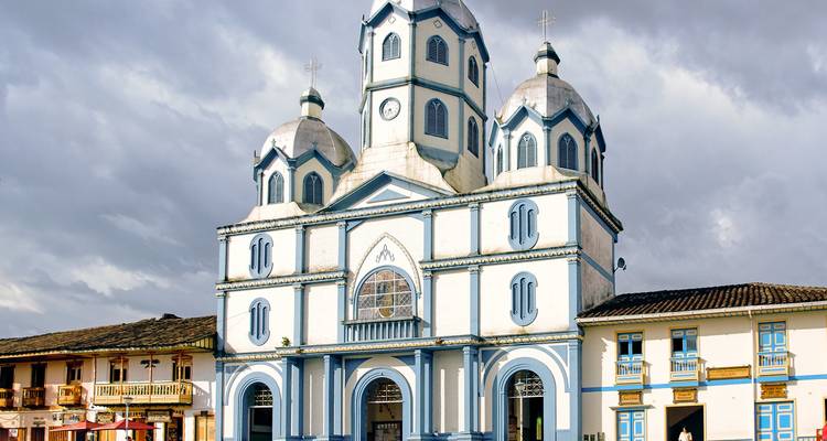 Iglesia colonial azul y blanca con cúpulas gemelas y fachada arqueada en una plaza del pueblo bajo cielos grises