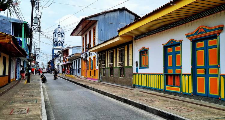 Vibrante calle colombiana bordeada de fachadas pintadas de colores brillantes y torre de iglesia distante en la región de Salento.