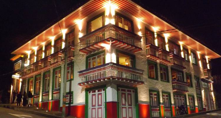 Vista nocturna de un edificio tradicional colombiano iluminado con luces cálidas en cada balcón.