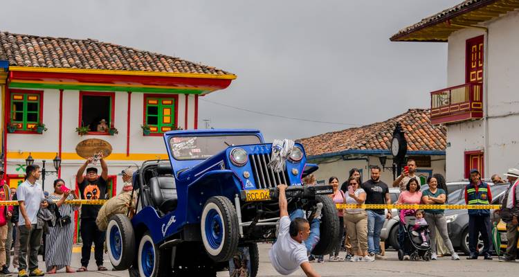 Un vieux Jeep bleu fait une roue arrière lors d'un festival municipal animé tandis que les spectateurs applaudissent.
