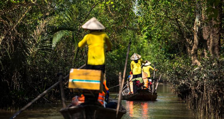 Des gens ramant dans des bateaux à travers un canal verdoyant.