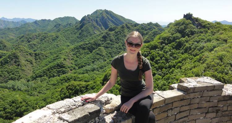 Persona sentada en la Gran Muralla China con exuberantes colinas verdes al fondo.