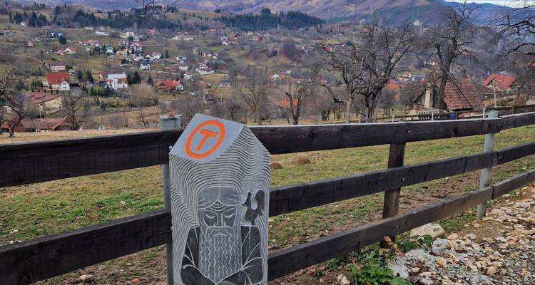 Vue de village en Roumanie avec un poteau de pierre sculptée au premier plan.