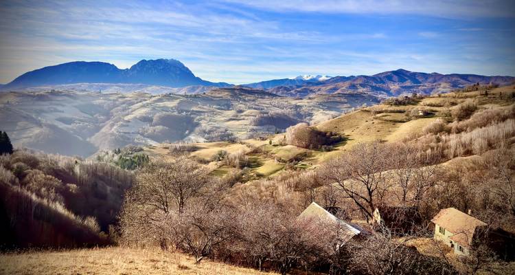 Paysage vallonné pittoresque avec des montagnes et quelques maisons éparses.