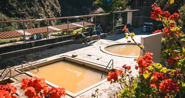 Una fuente termal al aire libre con algunas personas y flores rojas vibrantes en primer plano.