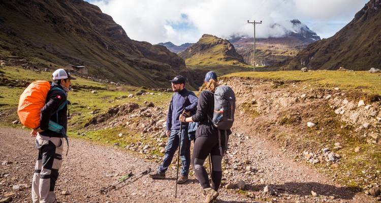 Tres excursionistas en un sendero de montaña con mochilas y bastones.