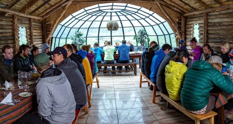 Groupe de personnes dînant à l'intérieur d'un chalet en bois avec de grandes fenêtres.