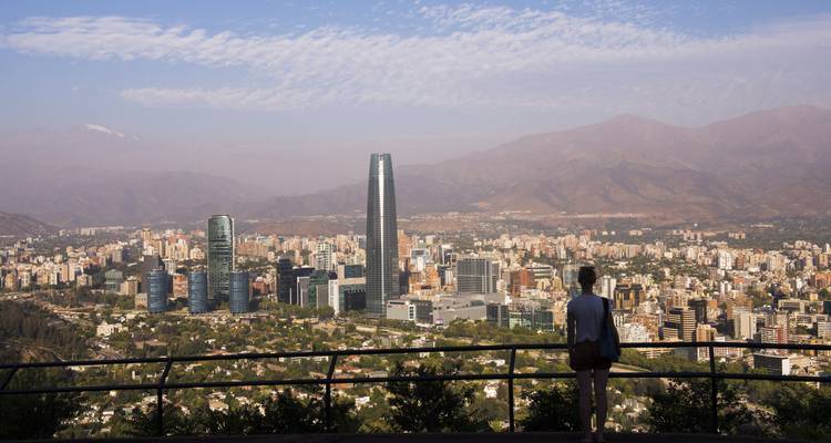 Person viewing a cityscape with modern skyscrapers and mountains in the background.