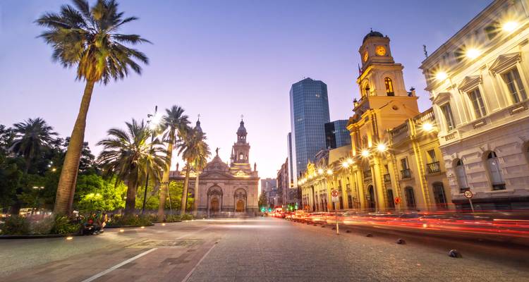 A bustling street at twilight with light trails and illuminated buildings.