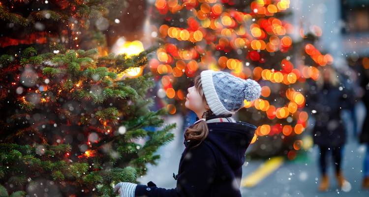 Niña pequeña admirando un árbol de Navidad durante una nevada.