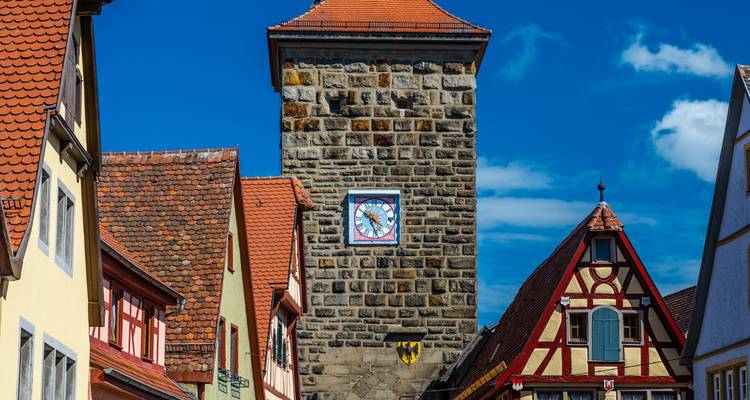 Torre del reloj de piedra que se alza sobre casas entramadas bajo un cielo azul profundo en Rothenburg ob der Tauber.