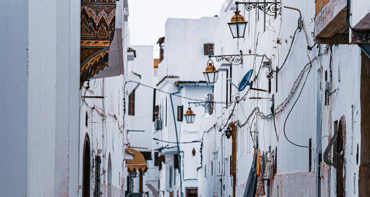 Schmale Gasse mit weißen Gebäuden und hängenden Laternen.