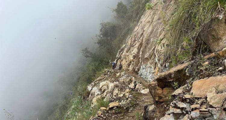 Randonneurs sur un sentier étroit sur une falaise brumeuse.
