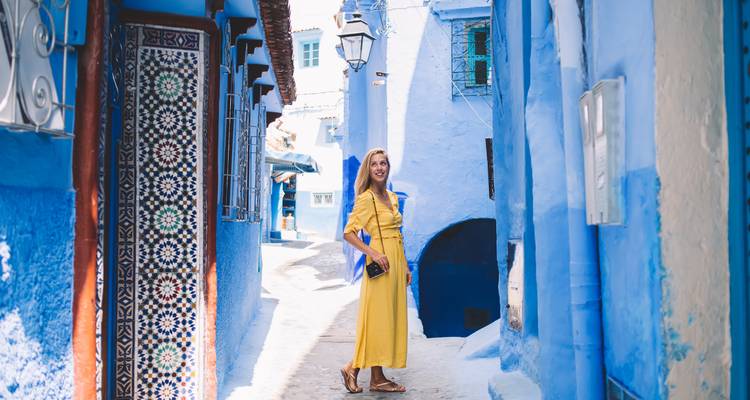 Une femme en robe jaune marchant dans une ruelle peinte en bleu.