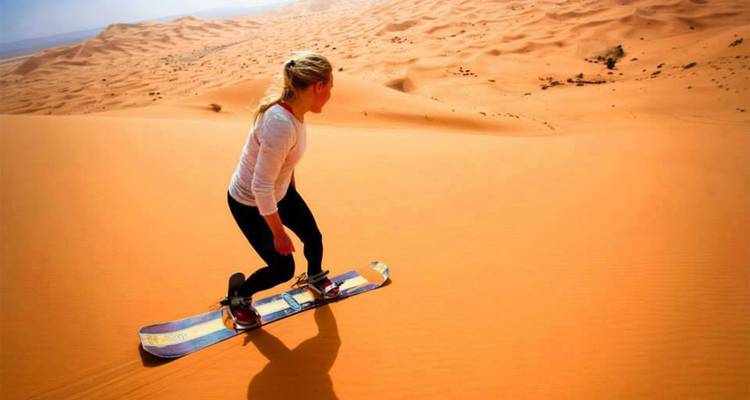 Personne faisant du sandboard sur une grande dune de sable.