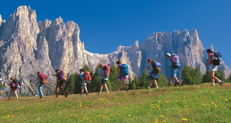 Grupo de senderistas caminando hacia los imponentes picos de las montañas en la distancia.