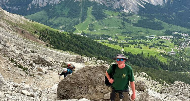 Mannelijke wandelaar klimt bergpad tussen rotsblokken met groene vallei ver beneden in de Dolomieten.