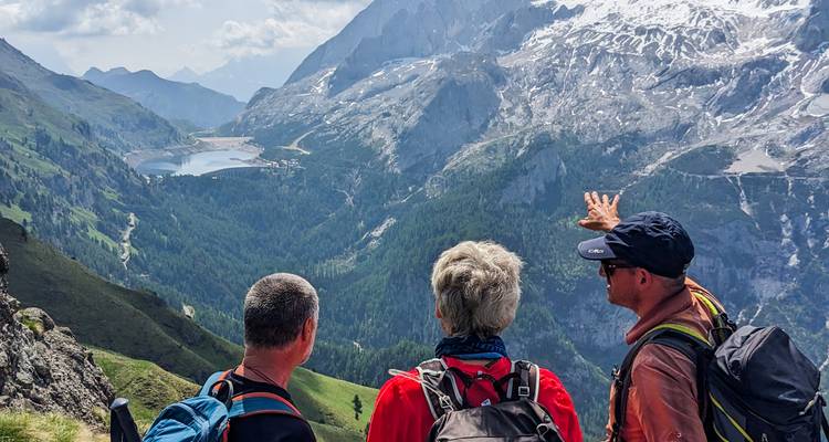 Wandelaars bewonderen het uitgestrekte alpiene dal en het meer onder besneeuwde bergtoppen.