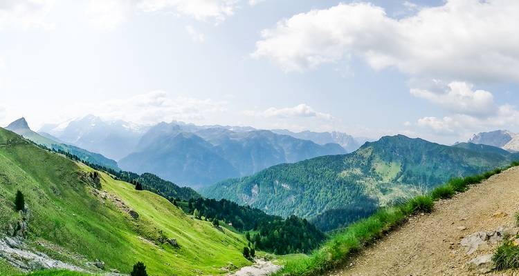Breed panorama van golvende alpine bergkammen en verre bergketens onder een gedeeltelijk bewolkte hemel.