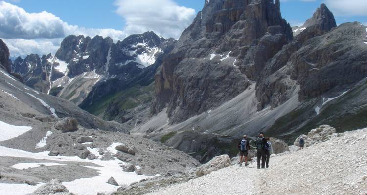 Senderistas caminando por un sendero de montaña rocoso con picos espectaculares.
