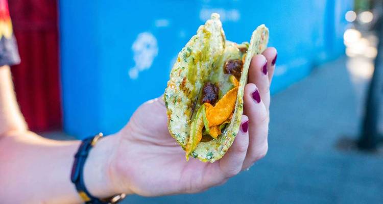 Main tenant un taco garni avec des éléments croustillants sur un fond bleu.