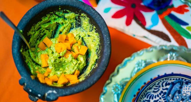 Bol de guacamole avec des morceaux de fruits hachés sur une table colorée.