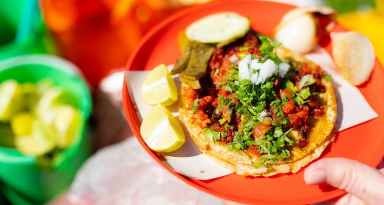 Taco garni de viande, d'herbes et de quartiers de lime sur une assiette rouge.