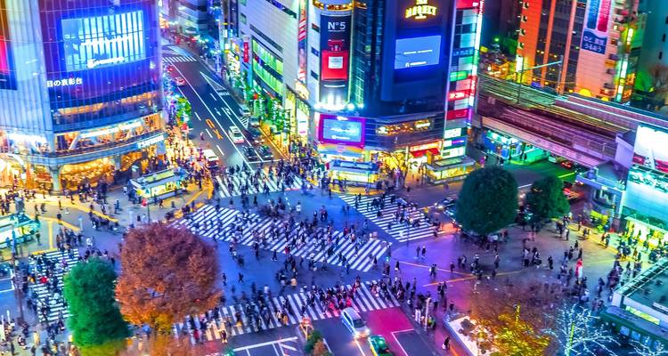 Intersection urbaine animée avec enseignes lumineuses la nuit.