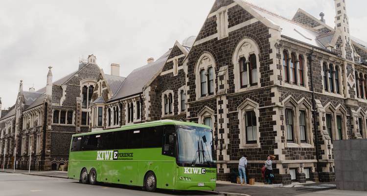 Autocar de tourisme garé devant des bâtiments historiques en pierre.