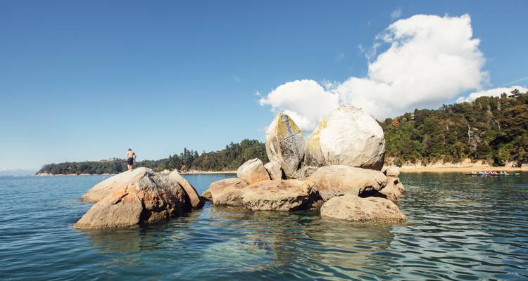 Personne debout sur des rochers au bord de la mer avec une forêt en arrière-plan.