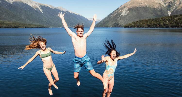 Trois personnes sautant dans un lac entouré de montagnes.