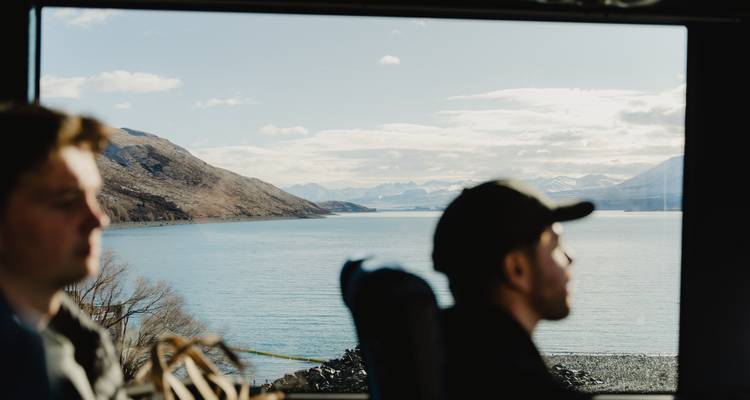 Vue floue de personnes dans un bus surplombant un lac et des montagnes.