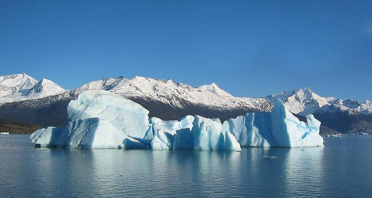 Icebergs flottants aux bords déchiquetés sur un lac bleu calme avec les Andes enneigées en arrière-plan sous un ciel dégagé